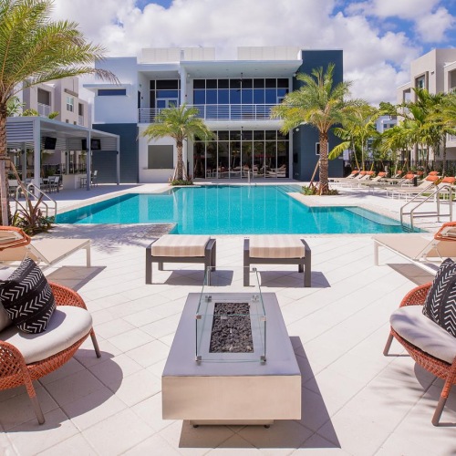a poolside patio with chairs and tables by it and a building in the background